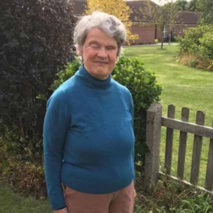 Eleanor stands in front of a hedge, smiling
