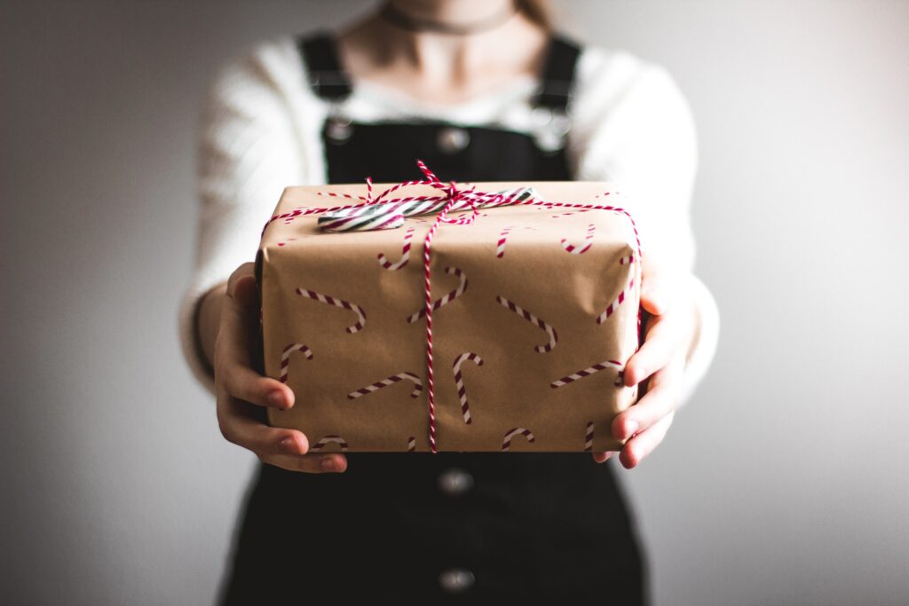 A person holding out a gift box wrapped in brown paper with a candy cane pattern on it