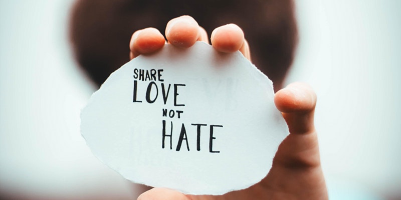 Hand holding a fragment of paper out in front of them that reads Share Love Not Hate