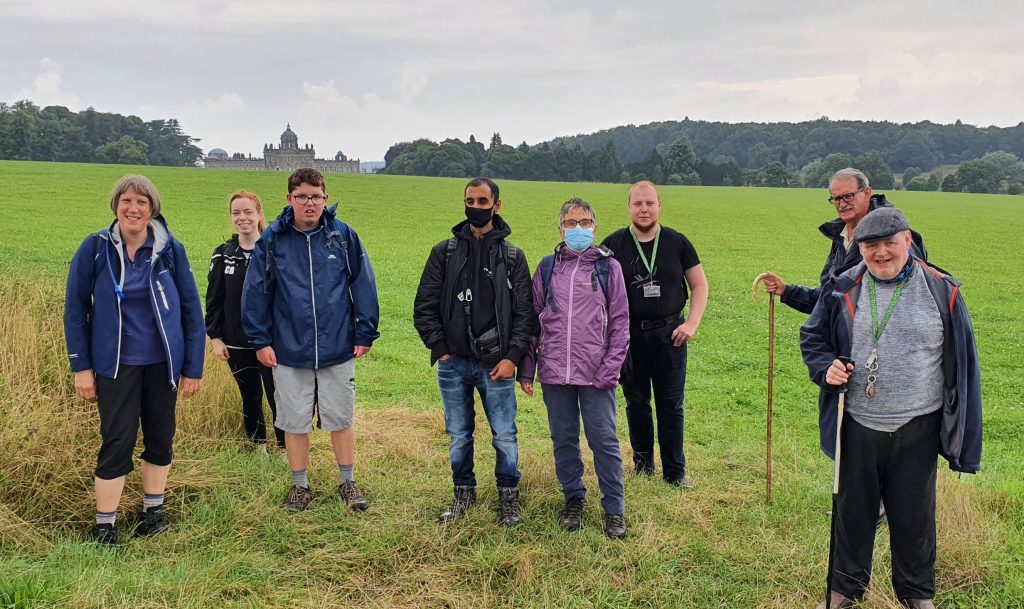 Group of walkers in a green field with a stately home in the distance